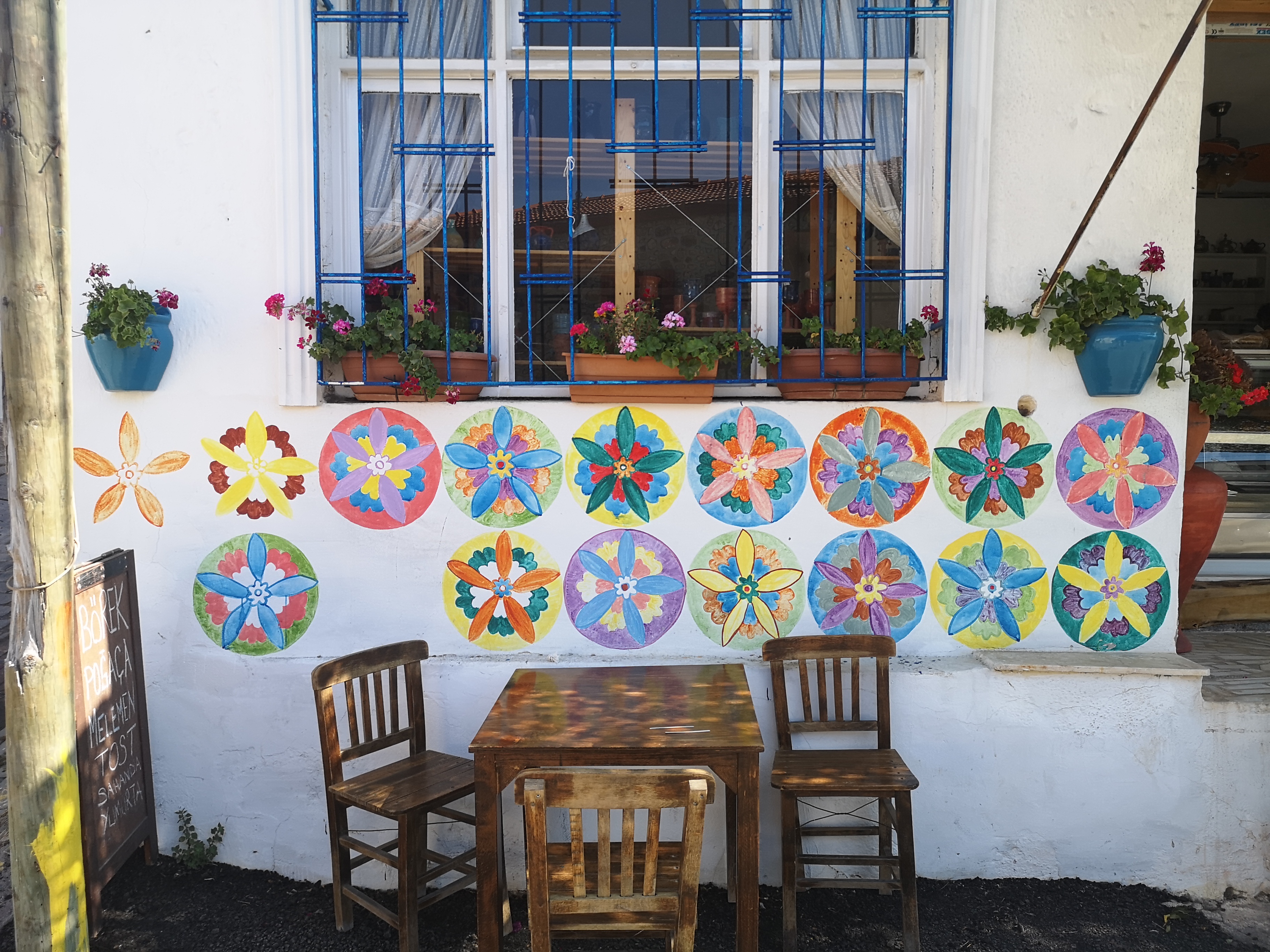 Gemalte Blumen, blaue Fenstergitter und Holzstühle vor einem Café im Dorf Germiyan.