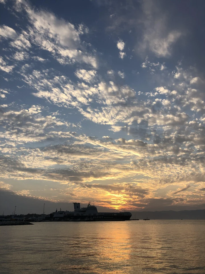 Çeşme kıyısında deniz üzerinde akşam bulutları ve gün batımı ışığı